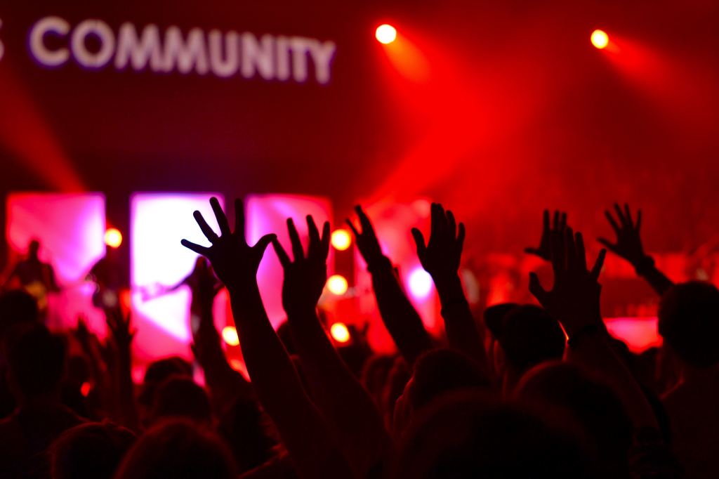 An indoor image, with the word 'community' in background and silhouettes of raised hands in foreground